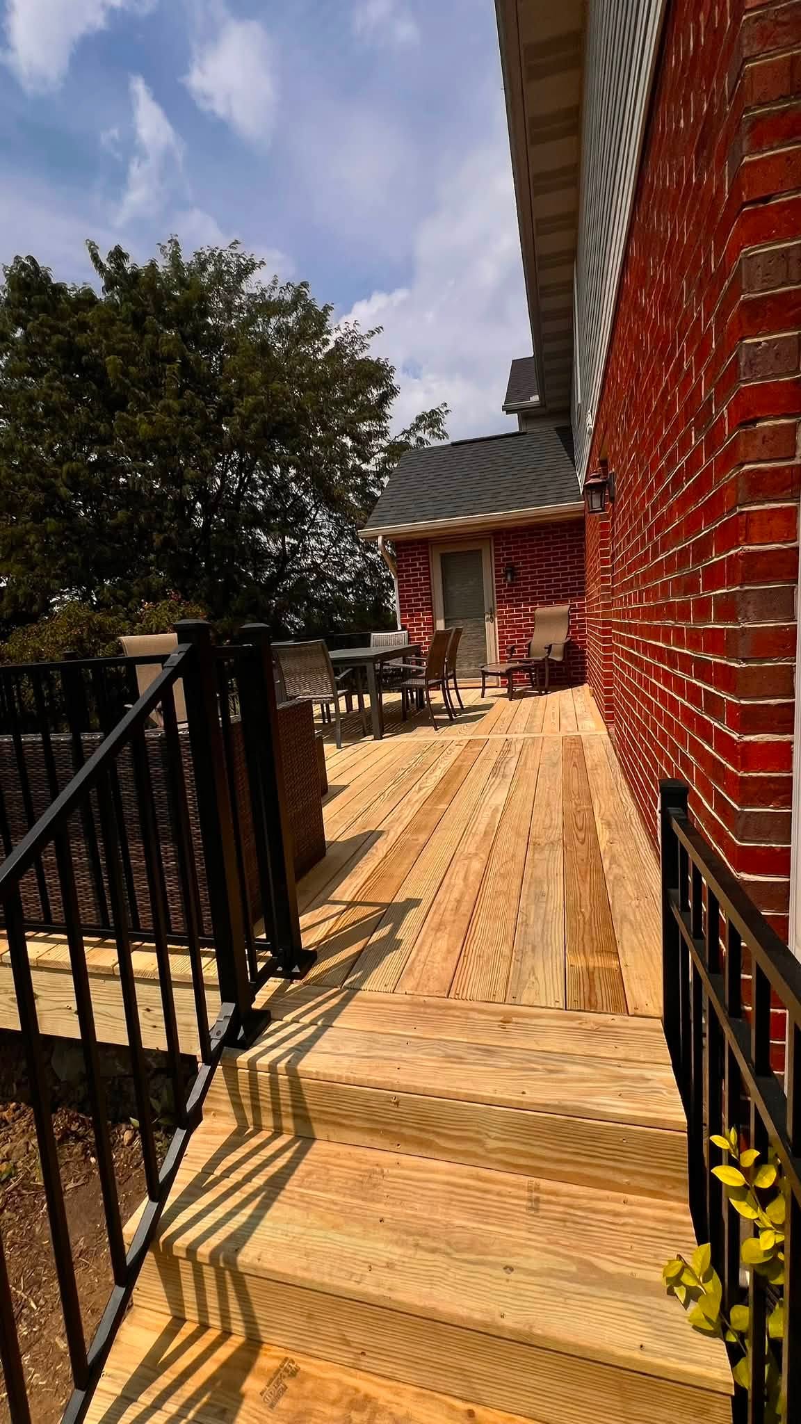Stained wood deck with black aluminum railing and steps at a brick home