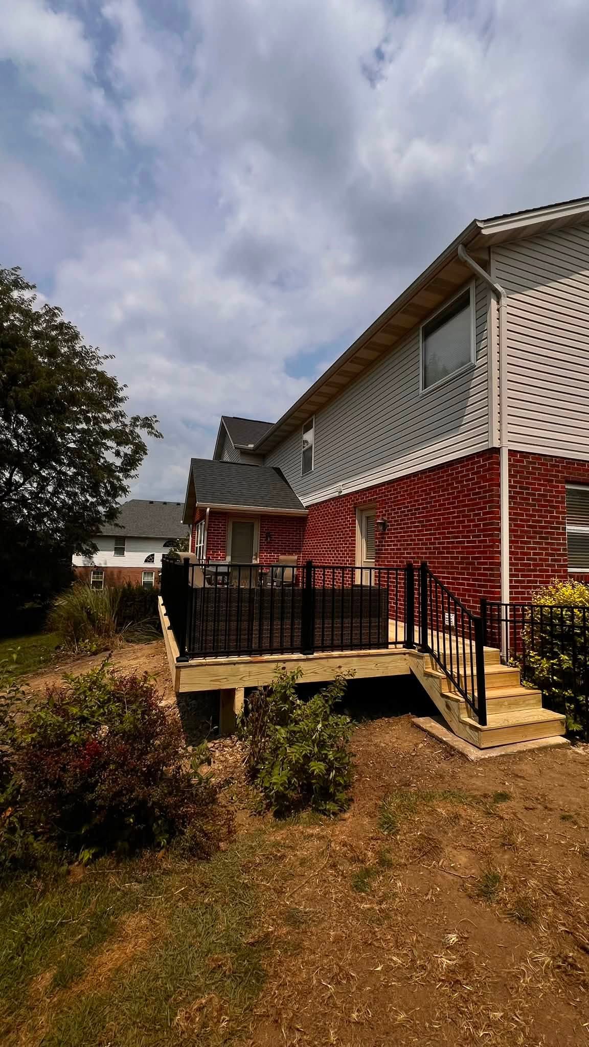 Pressure-treated wood deck with black railing behind a two-story brick home