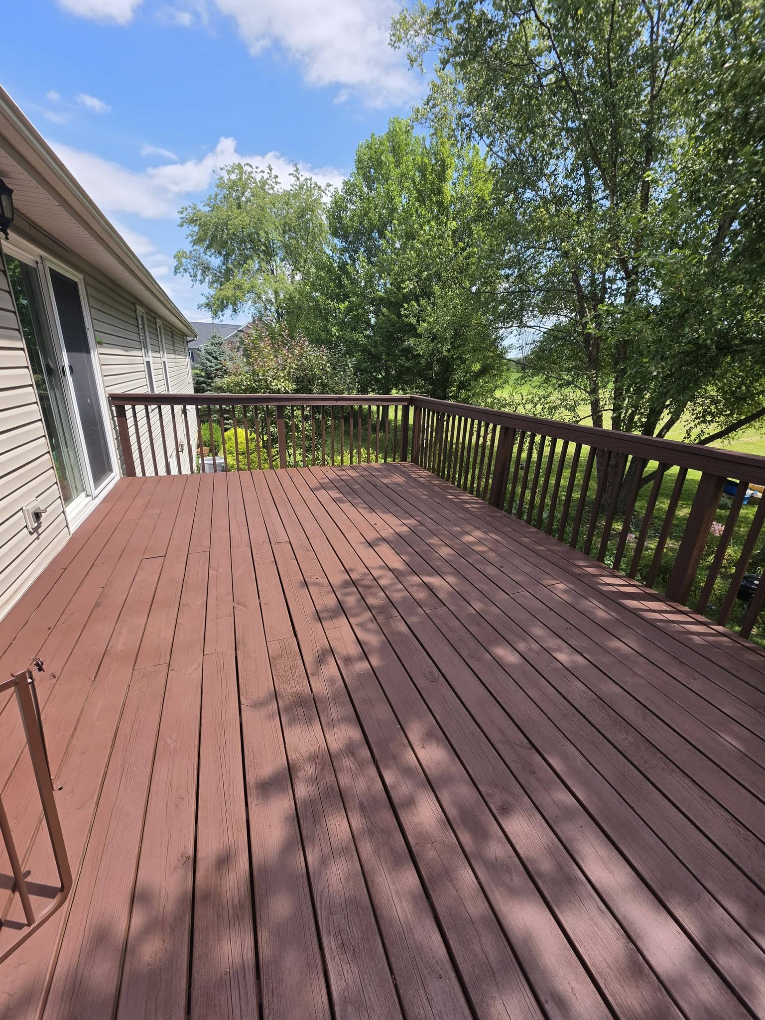 Dark red-stained wood deck with railing overlooking mature trees