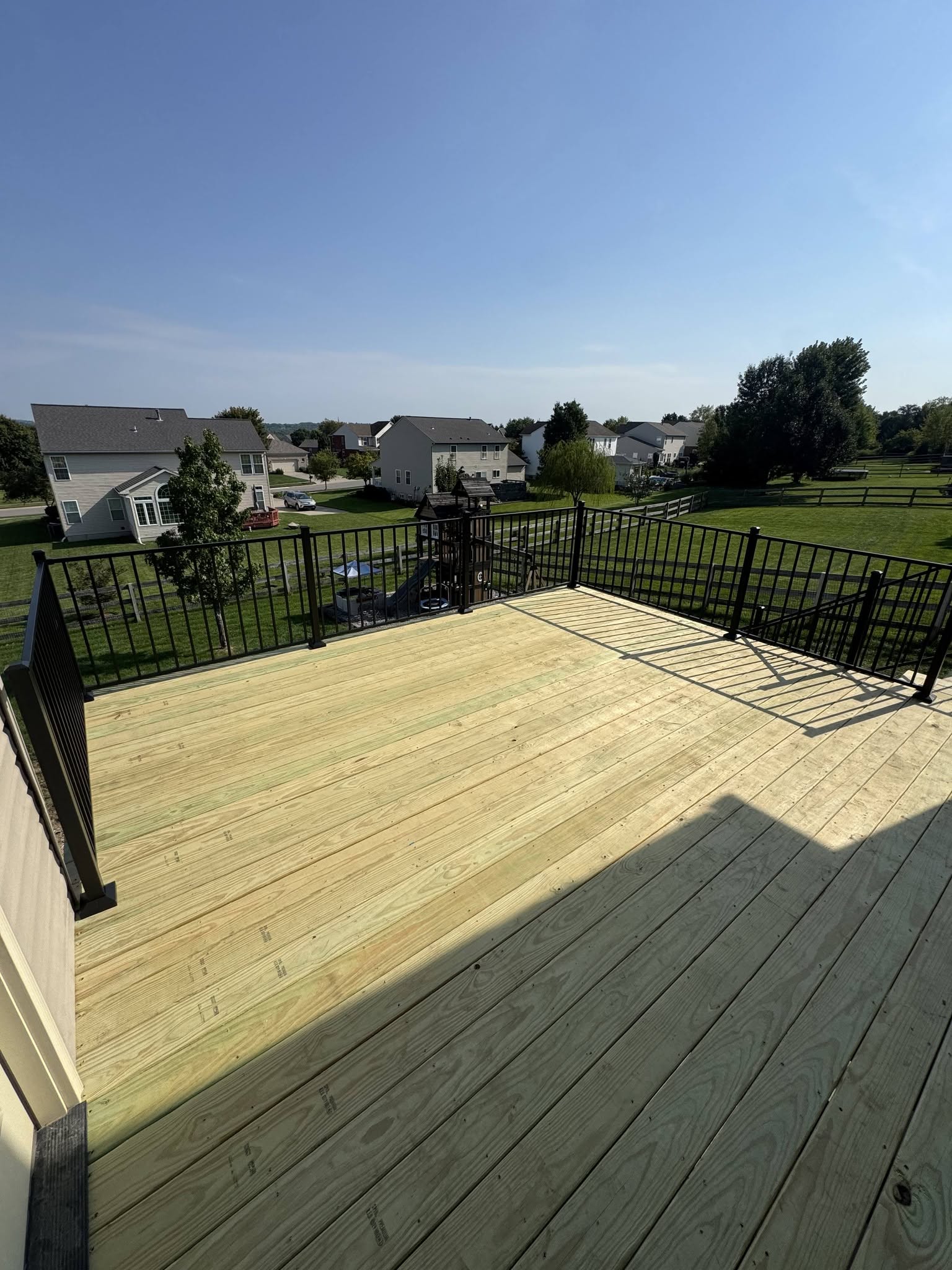 Raised pressure-treated wood deck with black aluminum railing overlooking a neighborhood