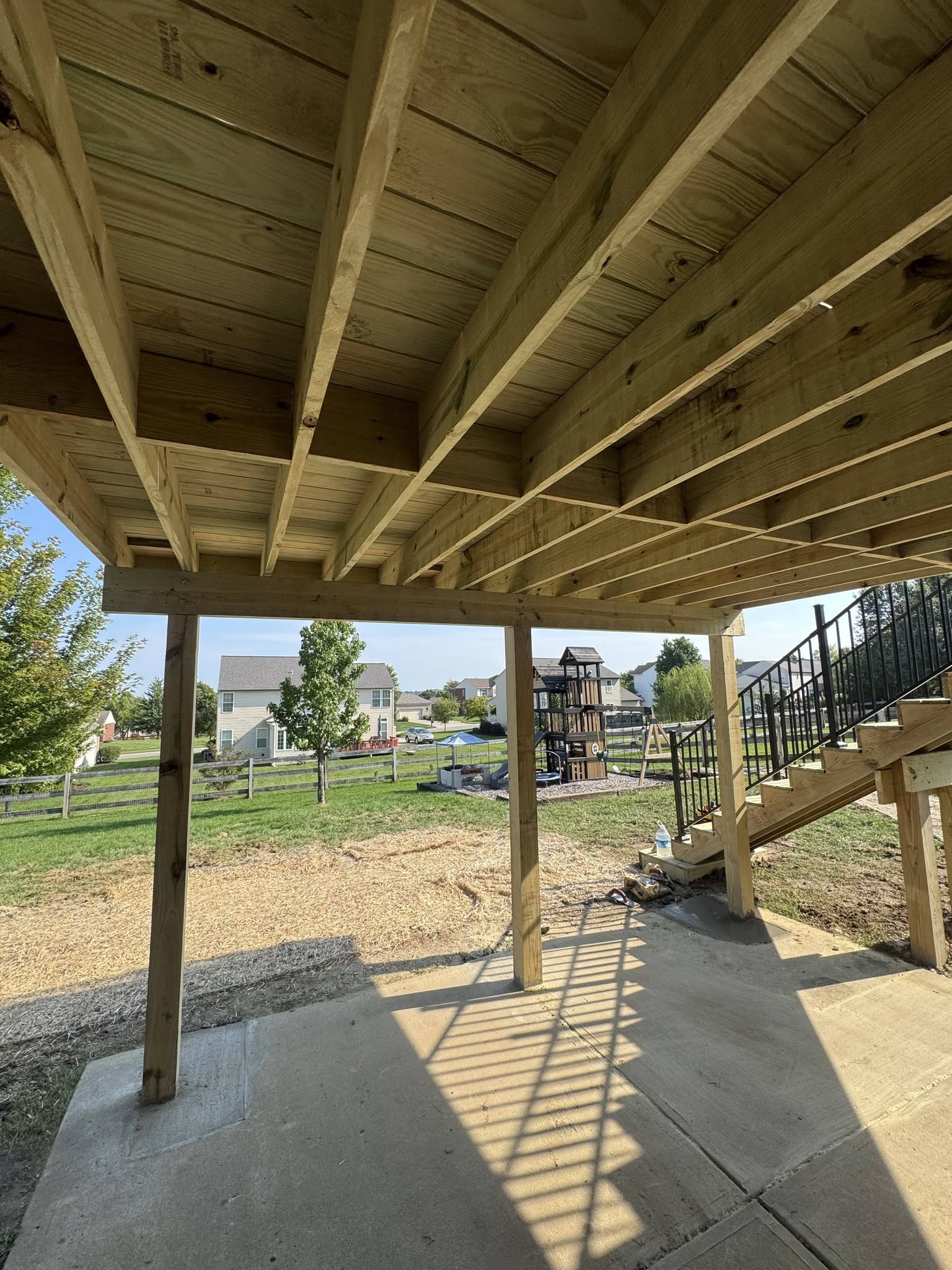 View beneath an elevated deck showing joists, posts and concrete patio