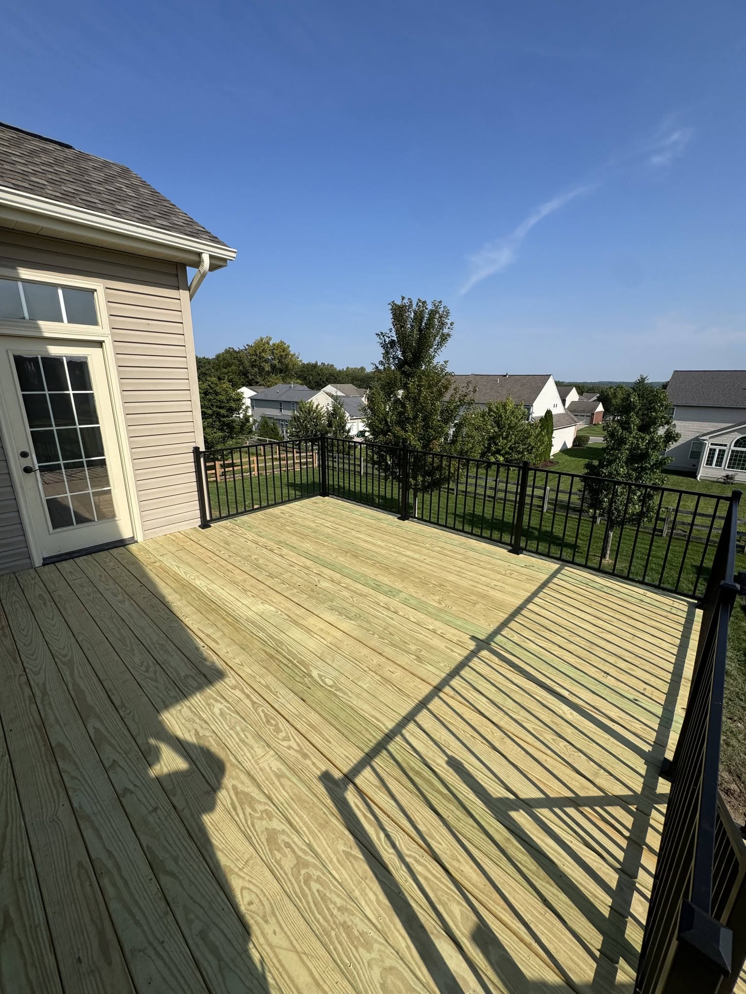 New pressure-treated wood deck with black aluminum railing beside a tan home